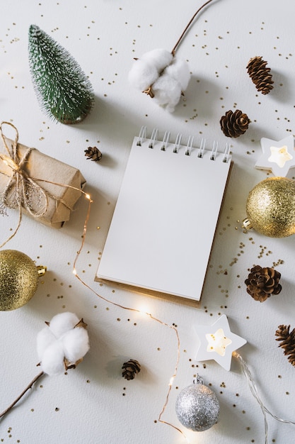 Christmas festive decorations and notebook. notebook, gift, and\
cotton branch with shiny golden balls.new year flat lay, top view,\
copy space.