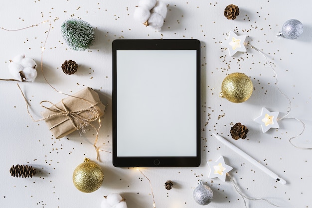 Christmas festive decorations and the tablet with pencil. With wish list and  goals concept. Tablet , gift, and coton branch with shiny golden balls.New year flat lay, top view, copy space.