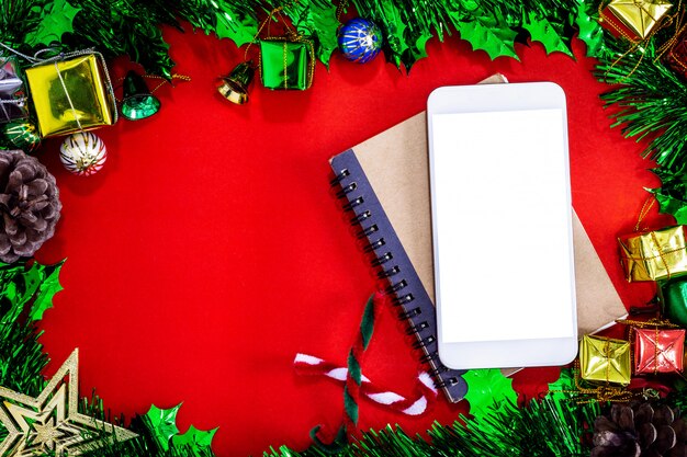 Christmas festive decorations with empty smartphone,notebook and pencil on red paper backg