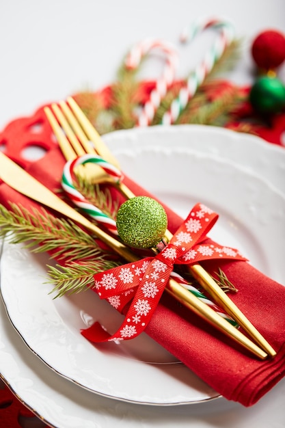 Christmas festive table setting with white plates and gold cutlery red linen napkin fir branches red