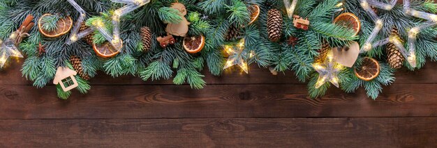 Christmas fir garland with natural decor, wooden toys and garland with lights on a wooden background.