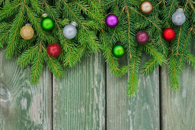 Christmas fir tree branches with colorful decoration on green wooden background. Copy space, top view