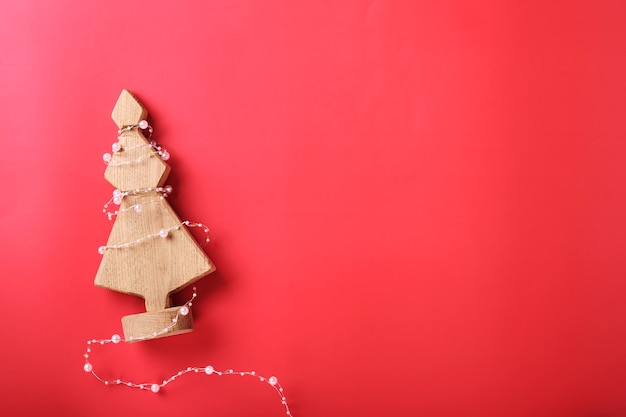 あなたのクリスマスの挨拶のための赤い背景の上のライトの美しい花輪と木から作られたクリスマスのモミの木。コピースペースのある上面図。クリスマスの背景。お祝いと装飾的なデザイン。