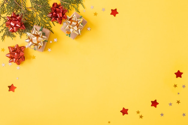 Christmas flat lay background. Gift boxes with glitters, decorations and star confetti on yellow.
