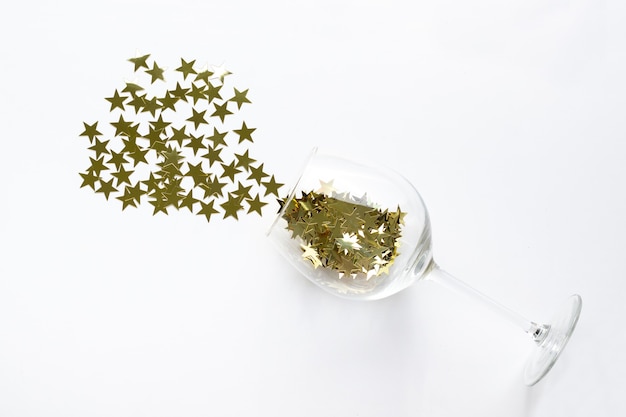 Christmas flat lay champagne glass poured out golden stars confetti with copy space. New Year Top view background