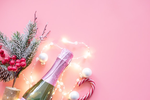 Christmas flat lay with champagne and garland on pink background. Christmas and New year background.