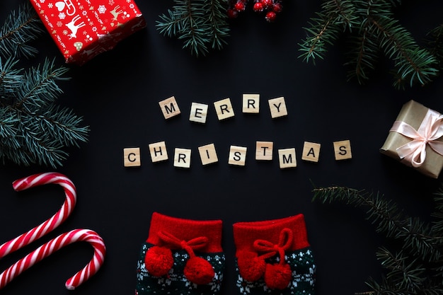 Christmas flat lay with Christmas tree branches, Christmas socks, gifts and wooden letters MERRY CHRISTMAS on black