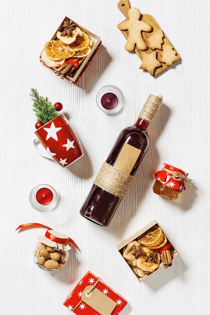 Christmas flat lay with Mulled wine Ingredients. Bottle red wine, red mug, paper gift box with spices, Christmas cookies, honey, almond, christmas decor. Preparation diy presents for winter holidays