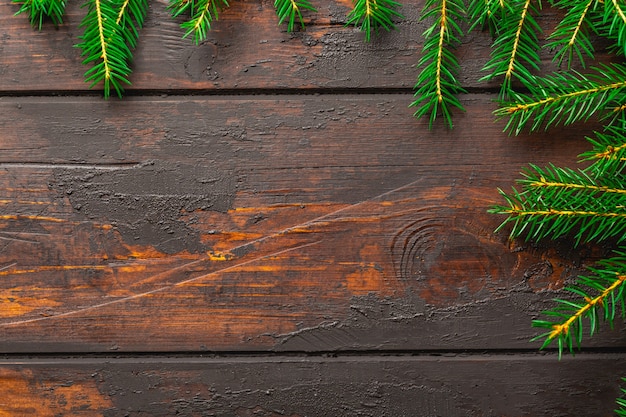 クリスマスフレームの背景。コピースペースのある茶色の素朴な木の板にクリスマスのモミの木の枝。