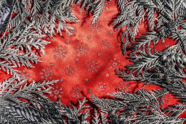 Christmas frame composition with silver thuja branches against red background. Overhead view, flat lay with copy space.