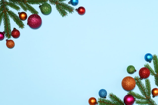 Christmas frame of fir branches and colored baubles on blue background
