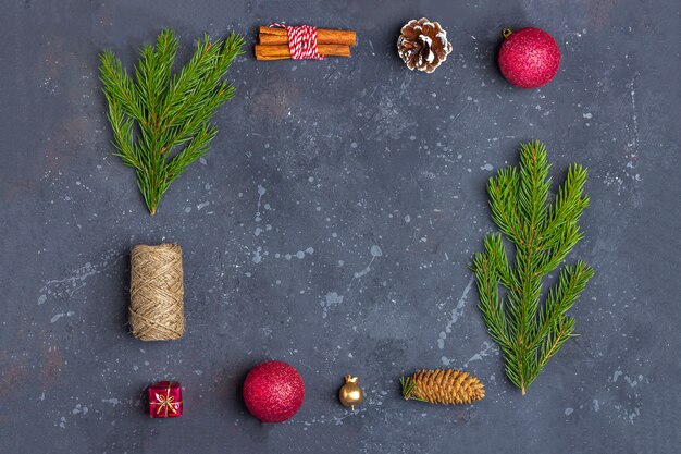 Christmas frame of fir branches, cone, cinnamon, rope and decoration on a dark background 