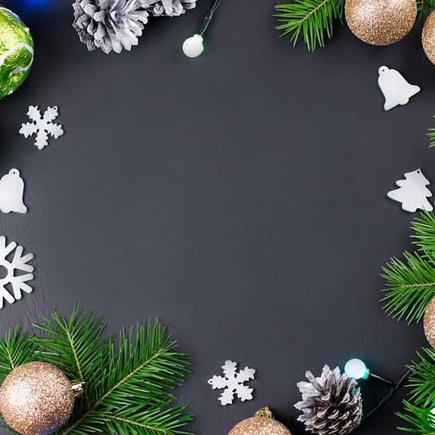 Christmas frame with fir branches, lights, golden and silver decorations on black wood. Copy space