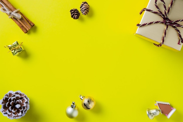 Рождественская рамка с подарочной коробкой, шишками, корицей и рождественскими украшениями на фоне желтой бумаги
