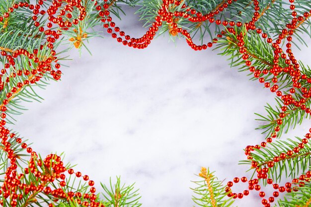 Christmas framework with fir branches and red beads on white background. Christmas frame of spruce branches on marble background. Red necklace. Copy space