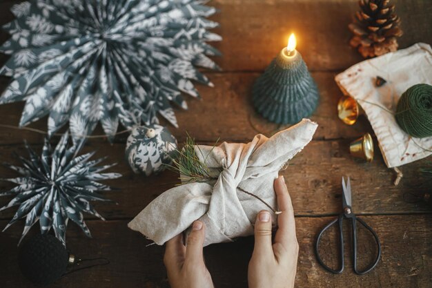 Christmas Furoshiki gift flat lay Hands holding gift wrapped in fabric on rustic table Zero waste