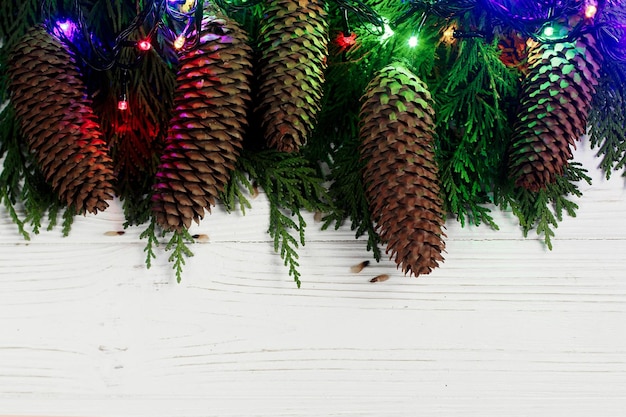 Photo christmas garland lights and pine cones on fir branches stylish white rustic wooden background space for text holiday greeting card concept unusual creative top view