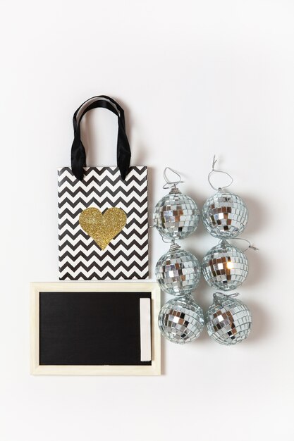 Photo christmas gift bag with gold heart, six little disco balls, chalk board on white wall, copy space. festive, new year, sales, shopping concept. vertical, flat lay. top view.