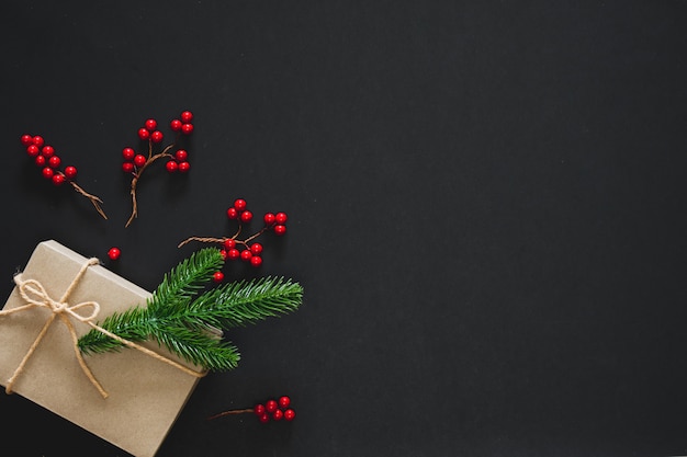 Photo christmas gift on black background with pine branches, berries and rope