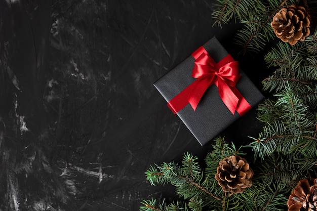 Christmas gift in black paper tied with red with pine branches and cones with place for text.