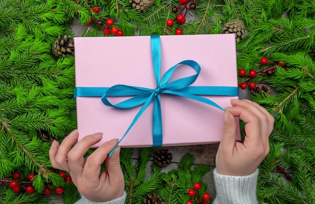 Christmas gift box in female hands Woman hands hold christmas or new year decorated gift box Christmas and New Year concept Womans hands open gift or present box decorated fir branches on table