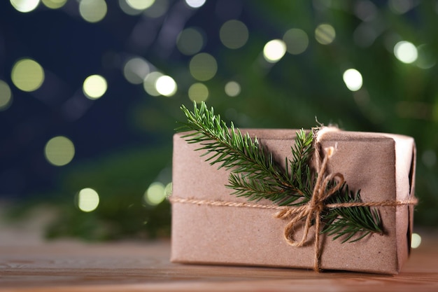 Christmas gift box in natural rough paper with spruce branch on bokeh background