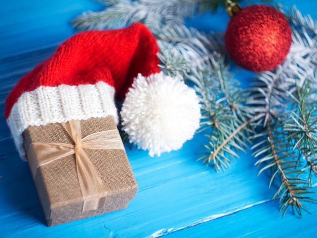 Christmas gift box in Santa hat on table with Christmas tree branches