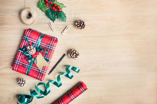 Foto confezione regalo di natale in carta fantasia tartan con materiali da imballaggio su sfondo di legno