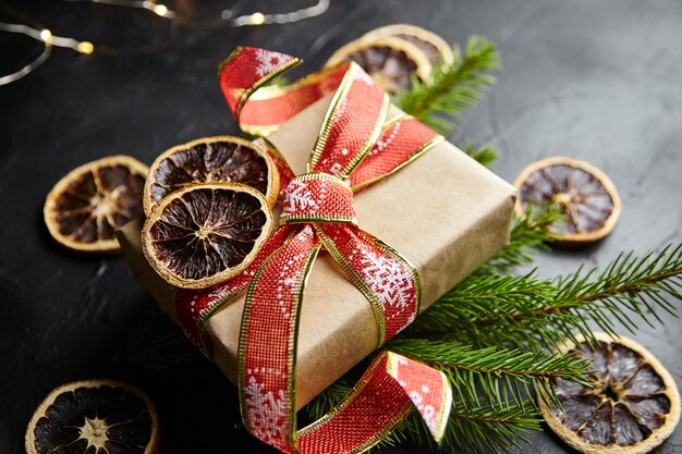 Christmas gift box with light garland and pine branches with dried orange fruit on black background