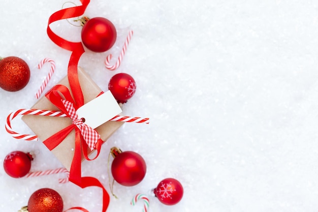 Christmas gift box with red ribbon balls and empty tag for text on the snow