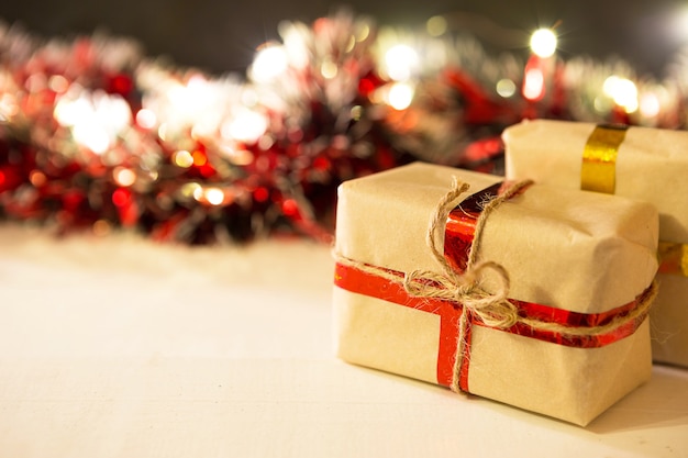 Christmas gift in a box wrapped in craft paper, tied with ribbon and rope, decorations with garland lights in a blur, red tinsel. New year. Background. Copy space