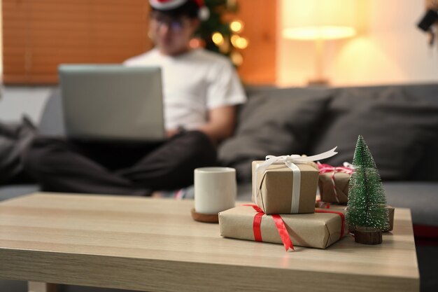 Christmas gift boxes and cup of coffee on wooden table in living room.