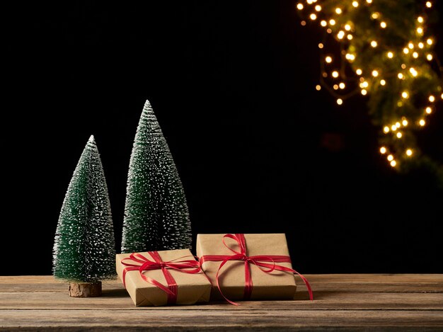 Christmas gift boxes and fir tree on wooden table against blurred festive lights, space for text