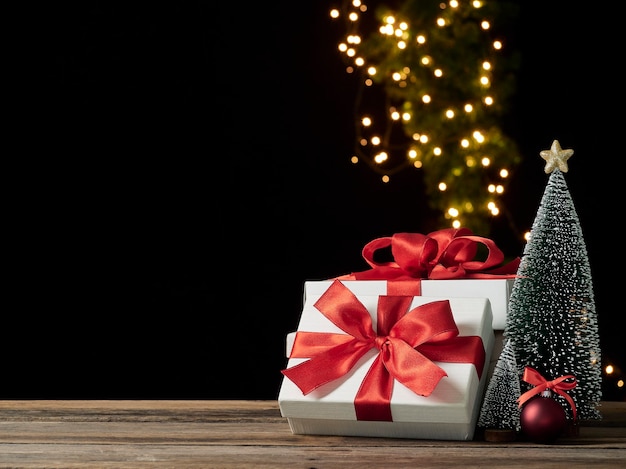 Рождественские подарочные коробки и елка на деревянном столе на фоне размытых праздничных огней, место для текста