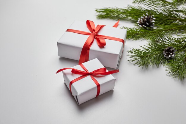 Christmas gift boxes with red ribbon and green pine tree branch with cones on white table