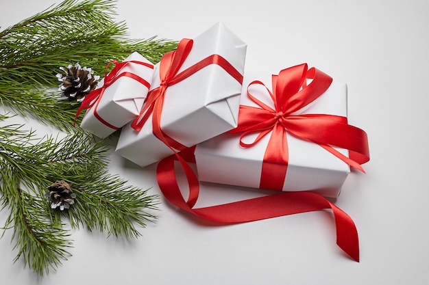 Christmas gift boxes with red ribbon and green pine tree branch with cones on white table