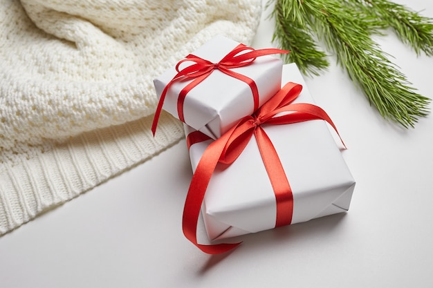 Рождественские подарочные коробки с красной лентой и вязаный свитер с зелеными ветками сосны на белом