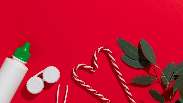 유칼립투스 잎과 사탕 지팡이가 있는 빨간색 배경에 안경 교정 콘택트 렌즈 렌즈 핀셋 및 콘택트 렌즈 솔루션을 위한 직원이 있는 크리스마스 선물 카드