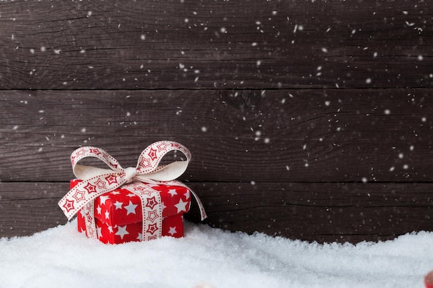 Christmas gift in snow over wooden background New Year's card