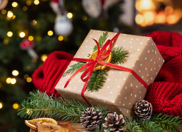 Christmas gift with bow near red sweater against burning fireplace and christmas tree lights