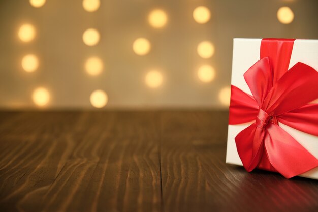 Christmas gift with red bow on one side of the image on an old brown wooden table with out of focus lights in the background