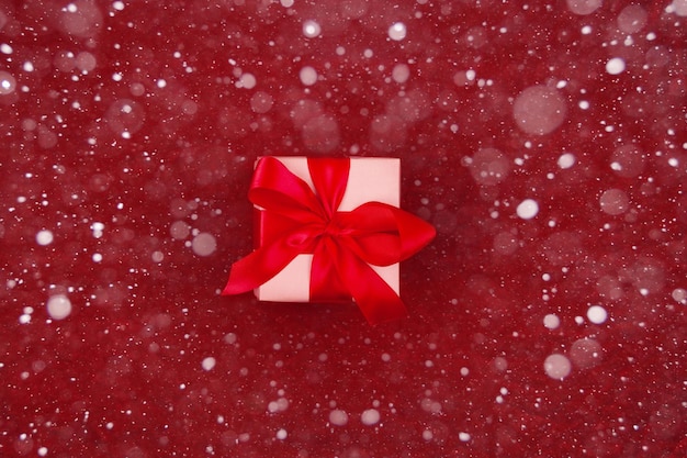 Christmas gift with red ribbon on red background with decorations