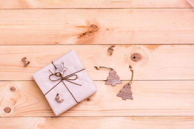 Christmas gift wrapped in craft paper and decorative trees on a natural wooden background. Eco-friendly Christmas concept. Copy space