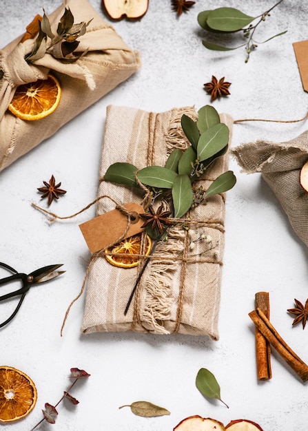 Christmas gift wrapped in linen cloth decorated with cinnamon sticks, dry apple and orange slices