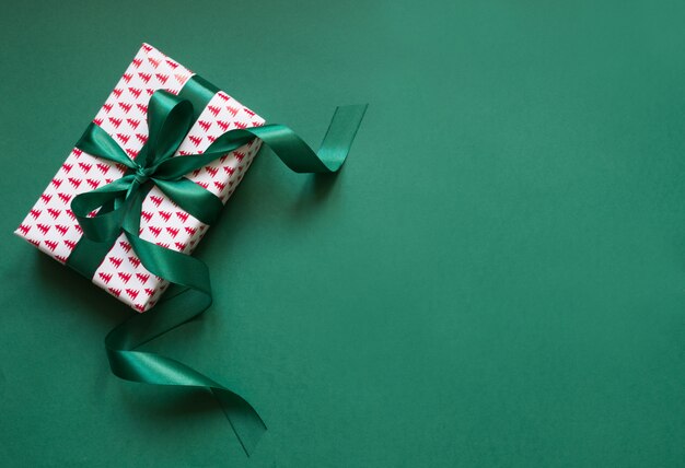 Christmas giftbox with green ribbon on green surface.  Holiday card.