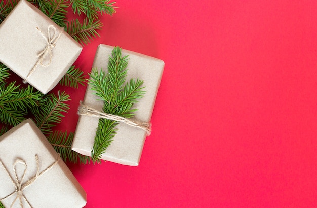 Рождественские подарки в крафт-бумаге и еловой ветке на красном фоне. безотходная упаковка для подарков