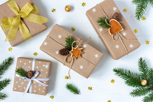 Christmas gifts in festive decor with eco twine and ribbon bows next to fir branches on white table