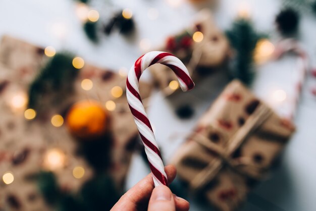 Christmas gifts, hand holds lollipop, tangerine on white wooden table.