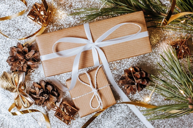 Christmas gifts in lights with pine cones and fir branches in a festive new year atmosphere on a silver background