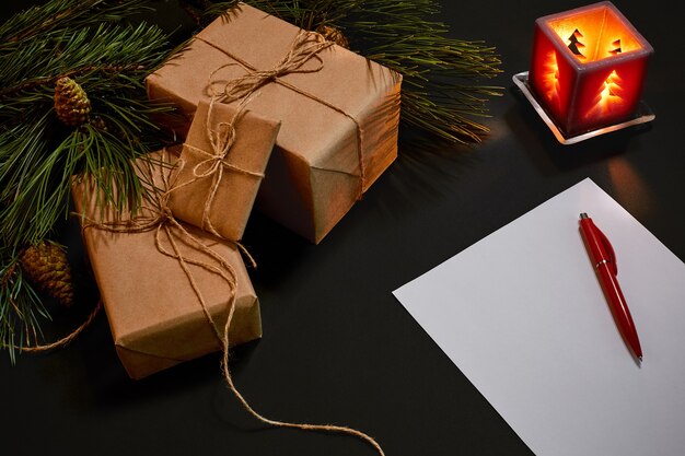 Christmas gifts and notebook lying near green spruce branch on black background top view. Copy space. Still life. Flat lay. New year
